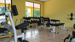 A gym with various exercise equipment, including dumbbells and weight benches, arranged in a spacious room with large windows. - Hospedaje Altamira (Florencia)