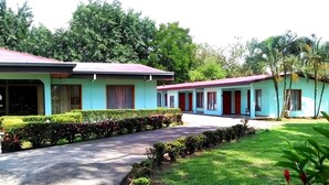 A row of light blue buildings with red roofs, surrounded by well-maintained greenery and a paved pathway. - Hospedaje Altamira (Florencia)