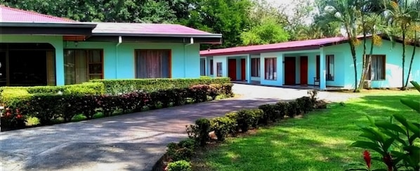 A building with a red roof and light blue walls, surrounded by well-maintained greenery and a paved driveway. - Hospedaje Altamira (Florencia)