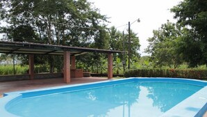 A rectangular swimming pool with a blue edge, surrounded by a brick patio and a covered area with a roof. - Hospedaje Altamira (Florencia)