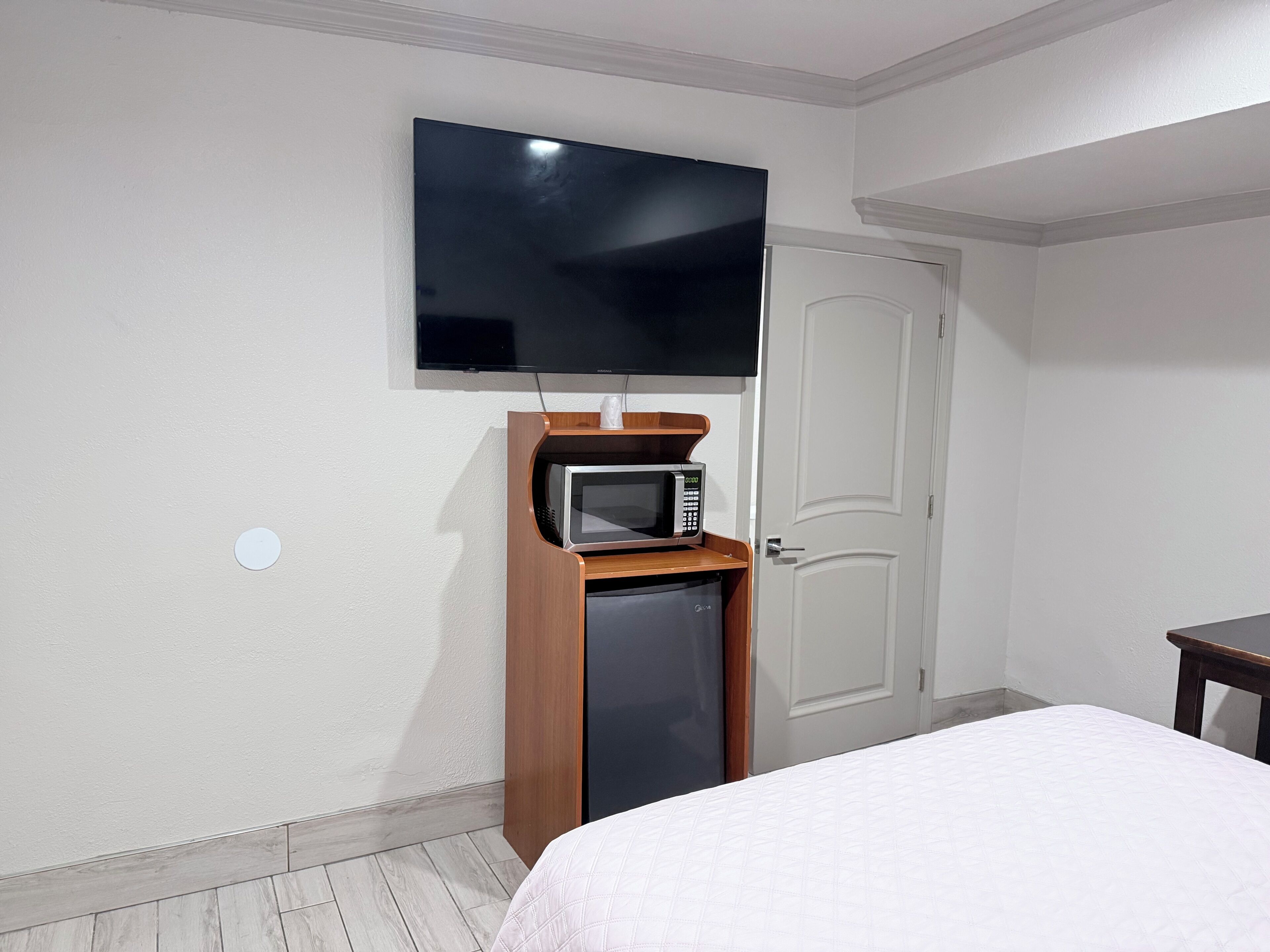 Habitación de hotel con cama, televisor montado en la pared, microondas y puerta.