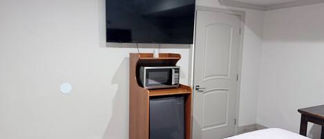 Habitación de hotel con cama, televisor montado en la pared, microondas y puerta.