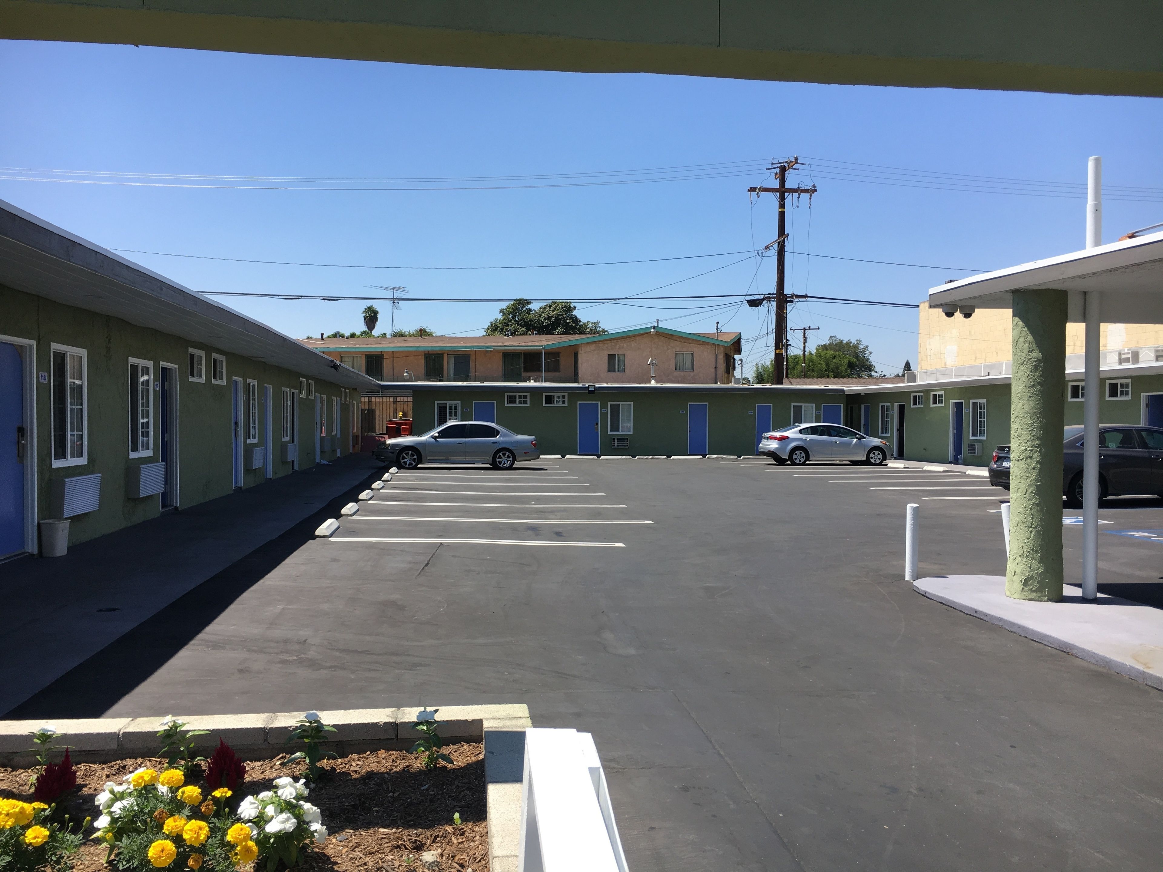 Ein Motel mit Parkplatz, eine Reihe von Zimmern mit blauen Türen und einem Gebäude im Hintergrund.