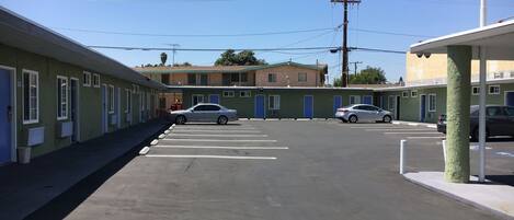 Ein Motel mit Parkplatz, eine Reihe von Zimmern mit blauen Türen und einem Gebäude im Hintergrund.