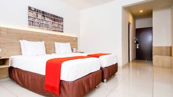 A modern hotel room with a large bed, two bedside tables, a bookshelf, and a door leading to another room.