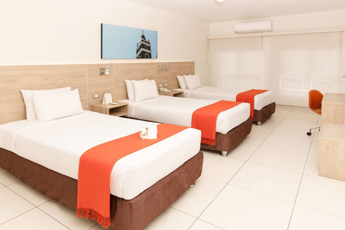 A hotel room with three beds, a desk, and a chair.