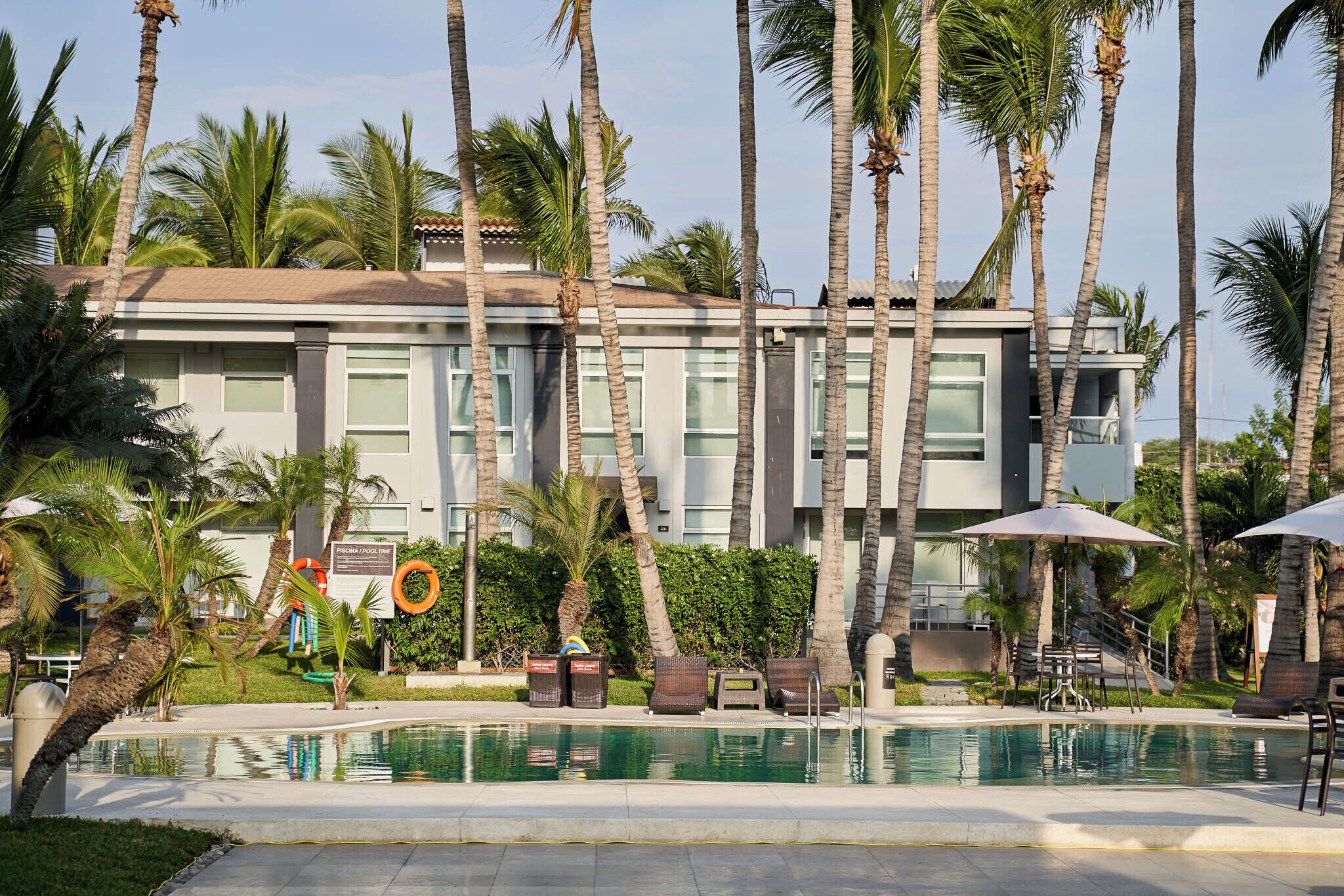 Un hotel moderno con piscina, palmeras y mobiliario al aire libre.