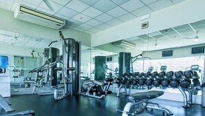 Un gimnasio con equipo de ejercicio, espejos y una barra de mancuernas.