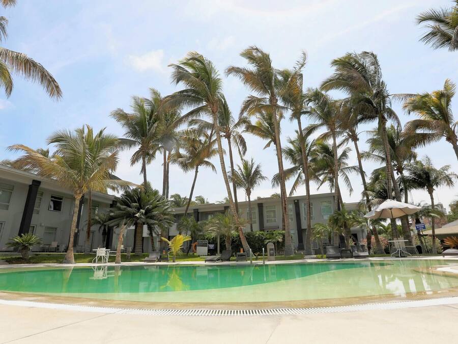 Ein Poolbereich mit Palmen, Liegestühlen und einem Gebäude im Hintergrund.