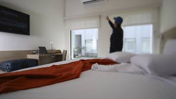 A hotel room with a bed, a desk with a laptop, a suitcase, and a TV mounted on the wall.