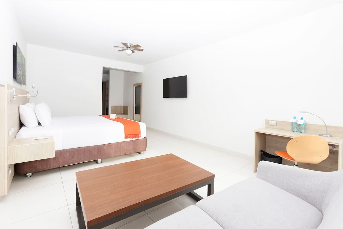 A modern hotel room with a bed, a desk, a chair, a sofa, and a ceiling fan.