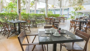 Un restaurante al aire libre con mesas preparadas para comer, rodeado de exuberante follaje y palmeras.