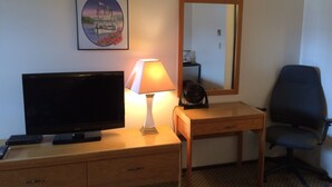 Une chambre d’hôtel avec un téléviseur posé sur une commode en bois, une lampe, un miroir et une chaise.