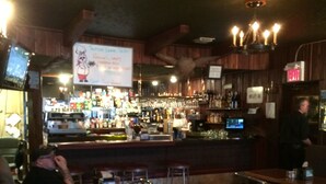 Un bar avec un mobilier en bois, un comptoir où sont exposées différentes bouteilles et un panneau de sortie lumineux.