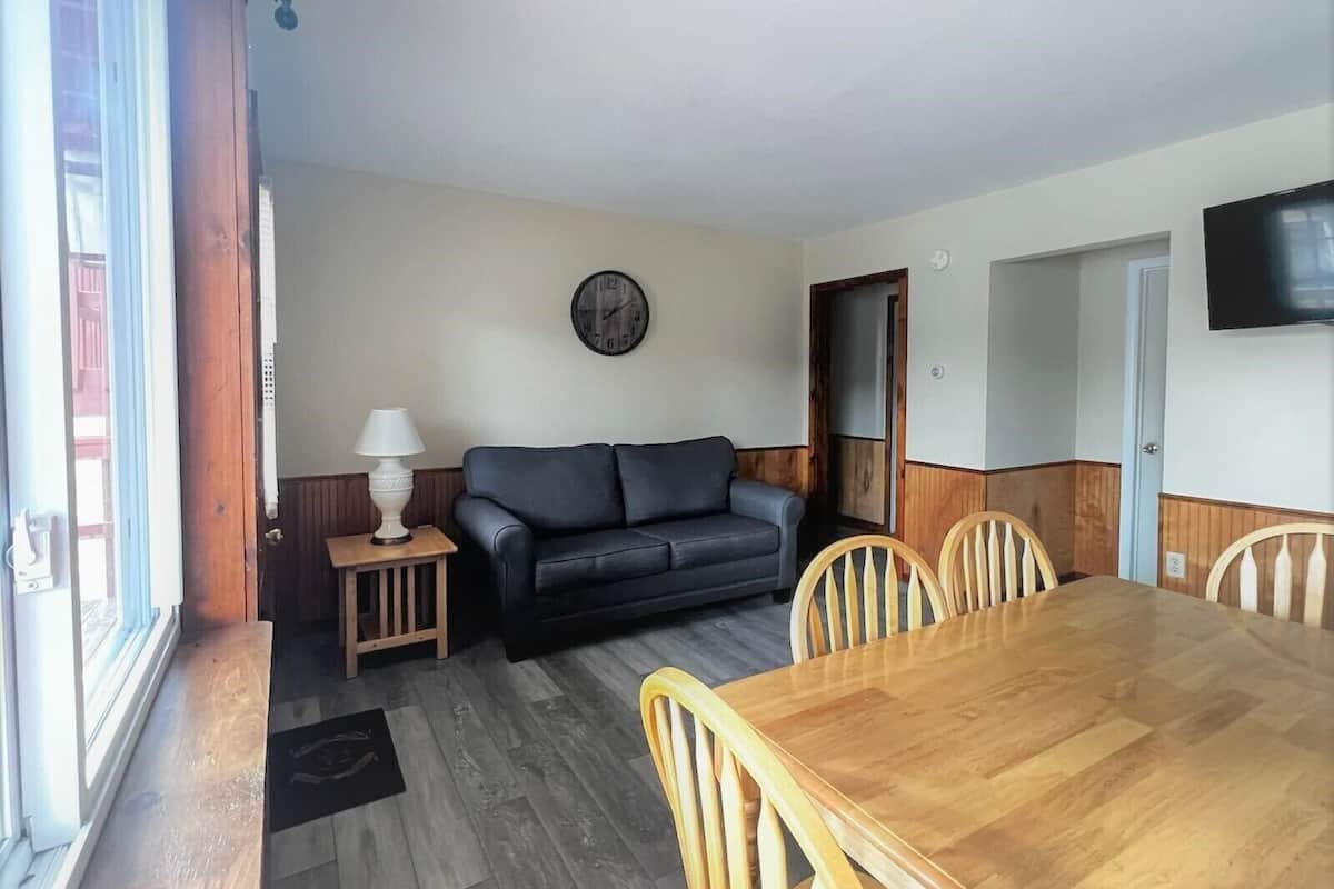 Un salon avec une table à manger en bois, un canapé noir et une chaise en bois.