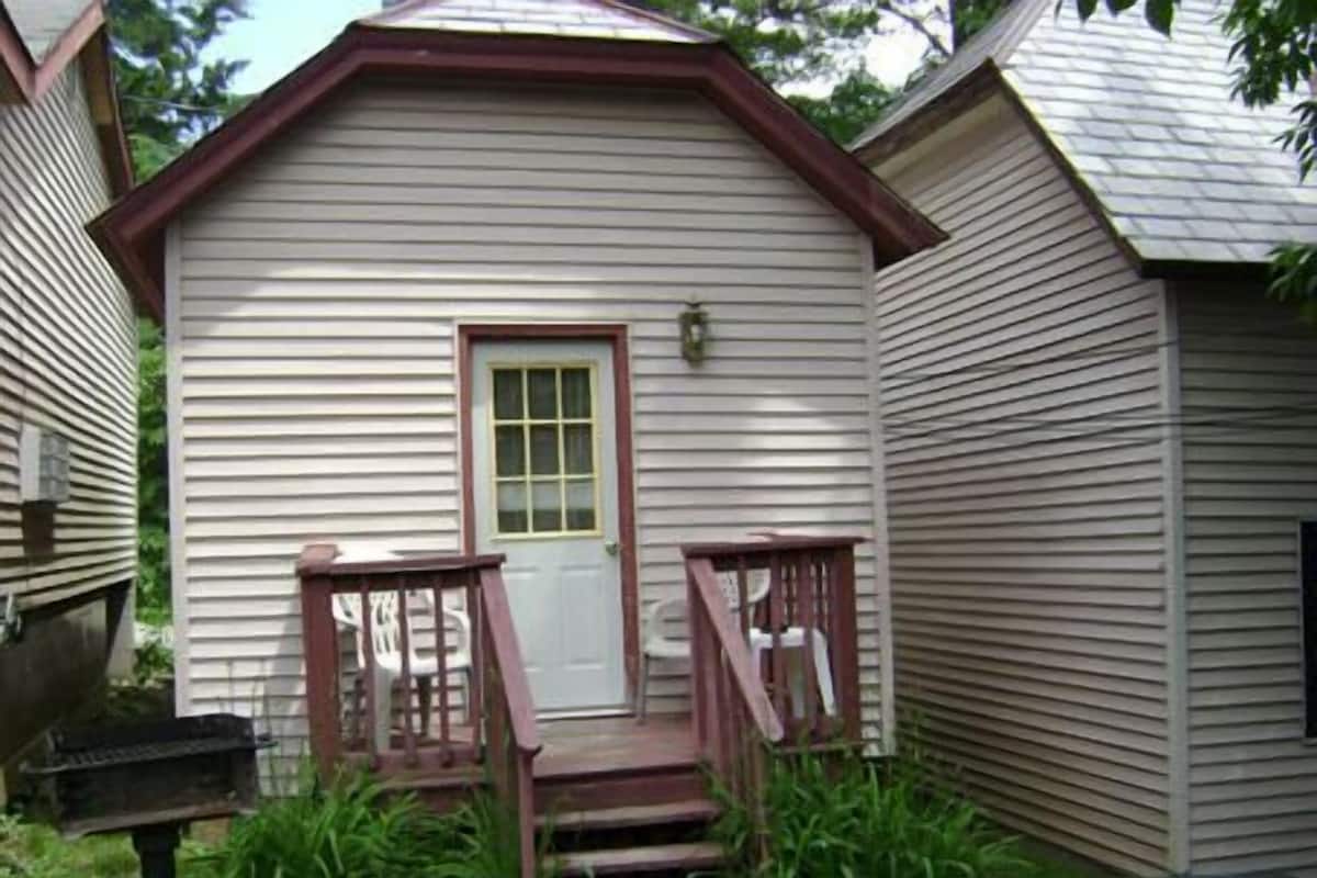 Une petite maison de plain-pied avec un porche à l’avant, une boîte aux lettres et un petit jardin.