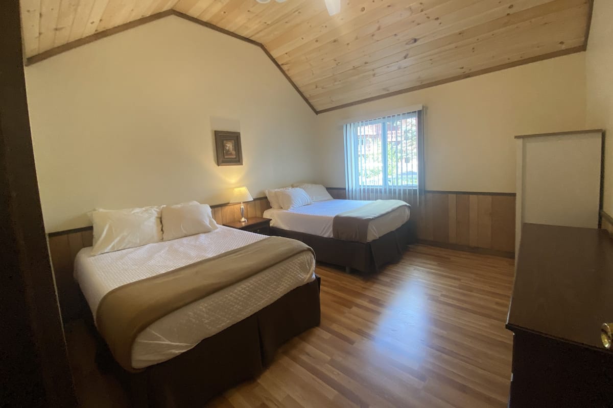 Une chambre avec deux lits, un plancher en bois, un ventilateur de plafond et une fenêtre avec des stores.