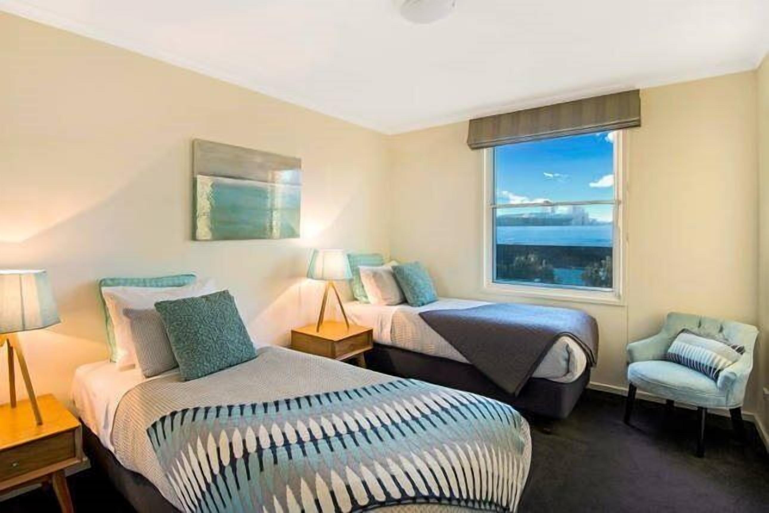 Een hotelkamer met twee bedden, een raam met uitzicht, een stoel en een lamp.