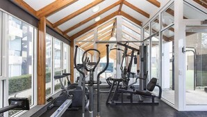 Un gimnasio con equipo de ejercicio, ventanas amplias y techo de madera.