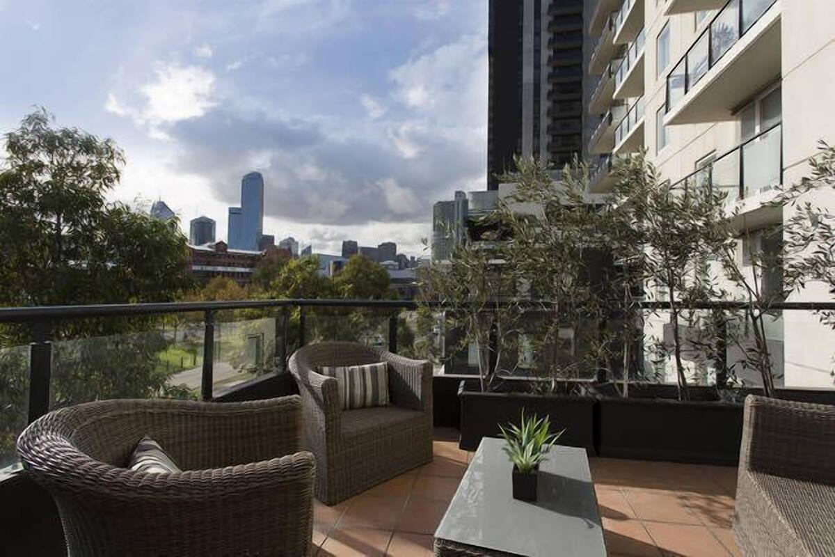 A rooftop terrace with wicker furniture, potted plants, and a city skyline view.