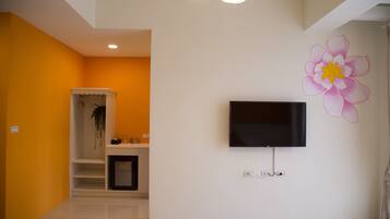 A modern living room with a flat-screen TV mounted on the wall, a large flower mural, and a white shelving unit with a hanging plant.