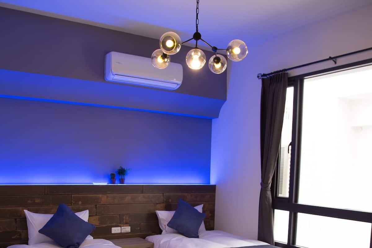 A modern hotel room with two beds, a large window, and a ceiling light fixture.
