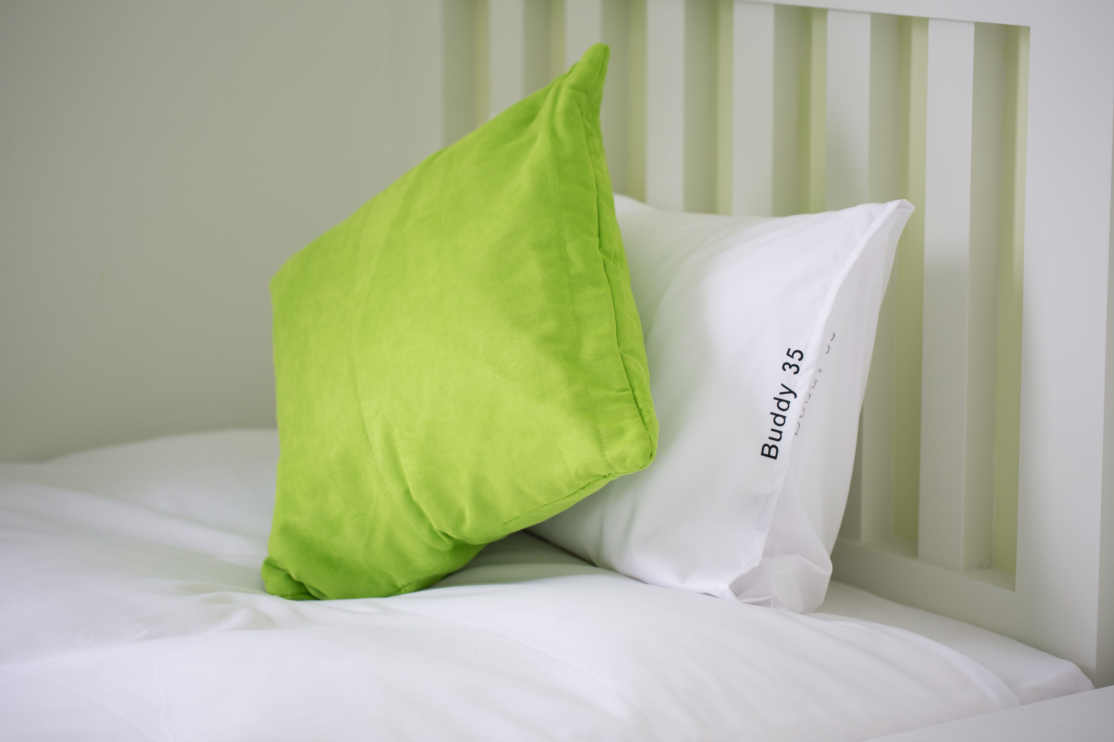 Una cama con ropa de cama blanca y una almohada verde.