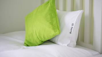 Una cama con ropa de cama blanca y una almohada verde.