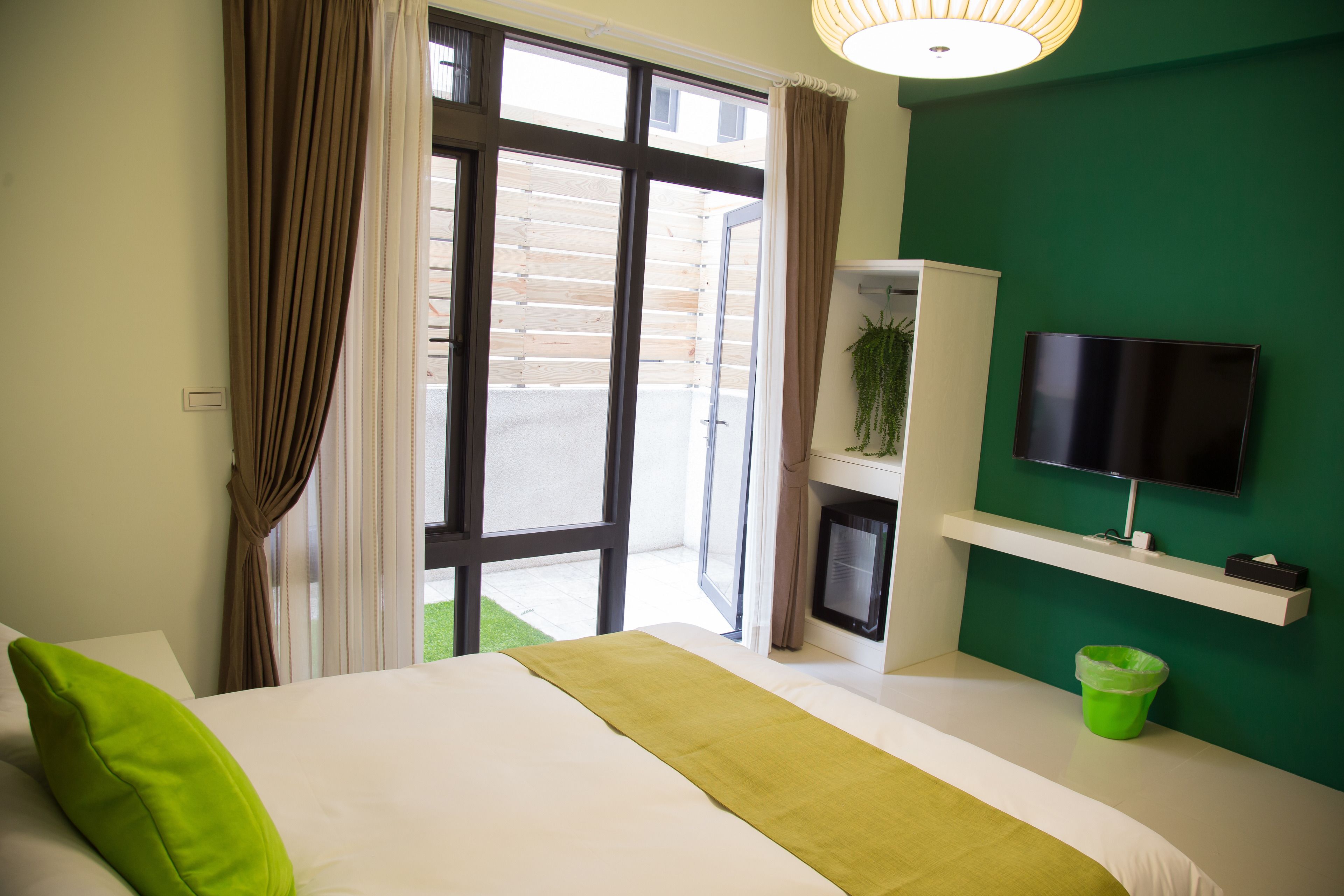 A hotel room with a bed, a television, a green wall, and a window with curtains.