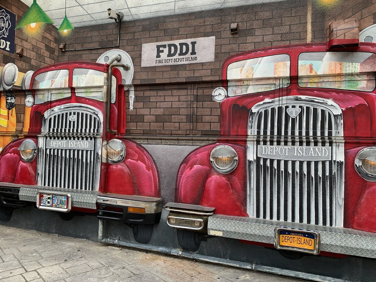 Drei Oldtimer-Feuerwagen sind in einer Reihe vor einer Ziegelwand geparkt, über ihnen ein Schild mit der Aufschrift 'FDDI FIRE DEPT DEPOT ISLAND'.