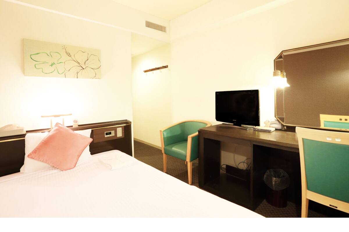 Een hotelkamer met een bed, een bureau met een computer, een stoel, een televisie en een lamp.
