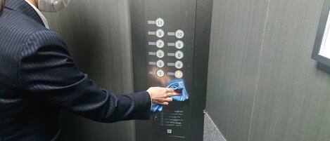 Une personne nettoie le panneau de commande d’un ascenseur à l’aide d’un chiffon bleu.