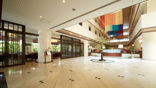 Een ruime lobby met een hoge plafond, een centraal gelegen receptiebalie en een groot raam met uitzicht op groen.