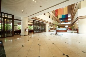 Un hall d’entrée spacieux avec un plafond haut, un comptoir d’accueil central et une grande fenêtre donnant sur un espace verdoyant.
