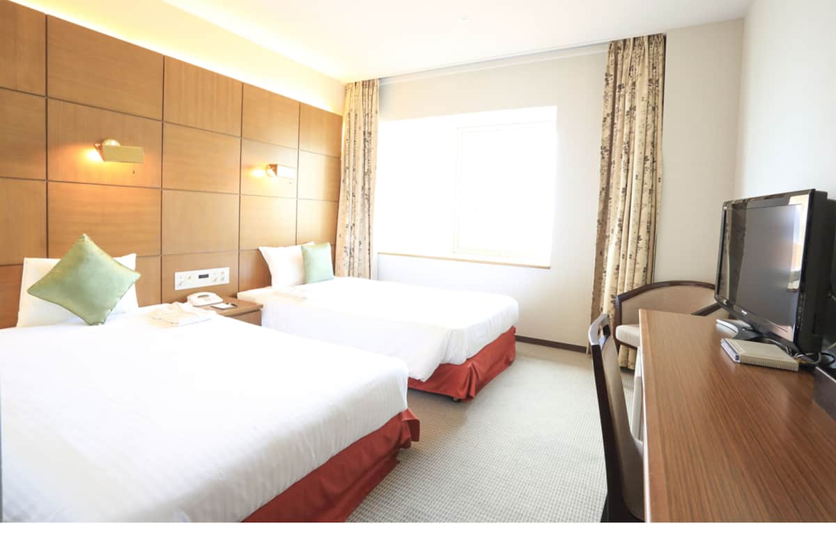 Een hotelkamer met twee bedden, een bureau, een televisie en een raam met gordijnen.