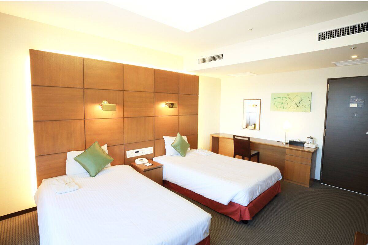 Een hotelkamer met twee bedden, een bureau, een stoel, een telefoon en een deur.