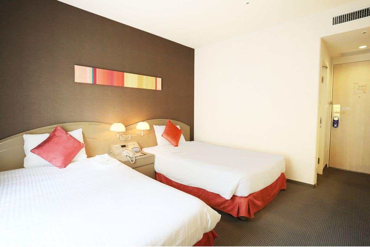 Een hotelkamer met twee bedden, een nachtkastje met een lamp, een telefoon en een kunstwerk aan de muur.