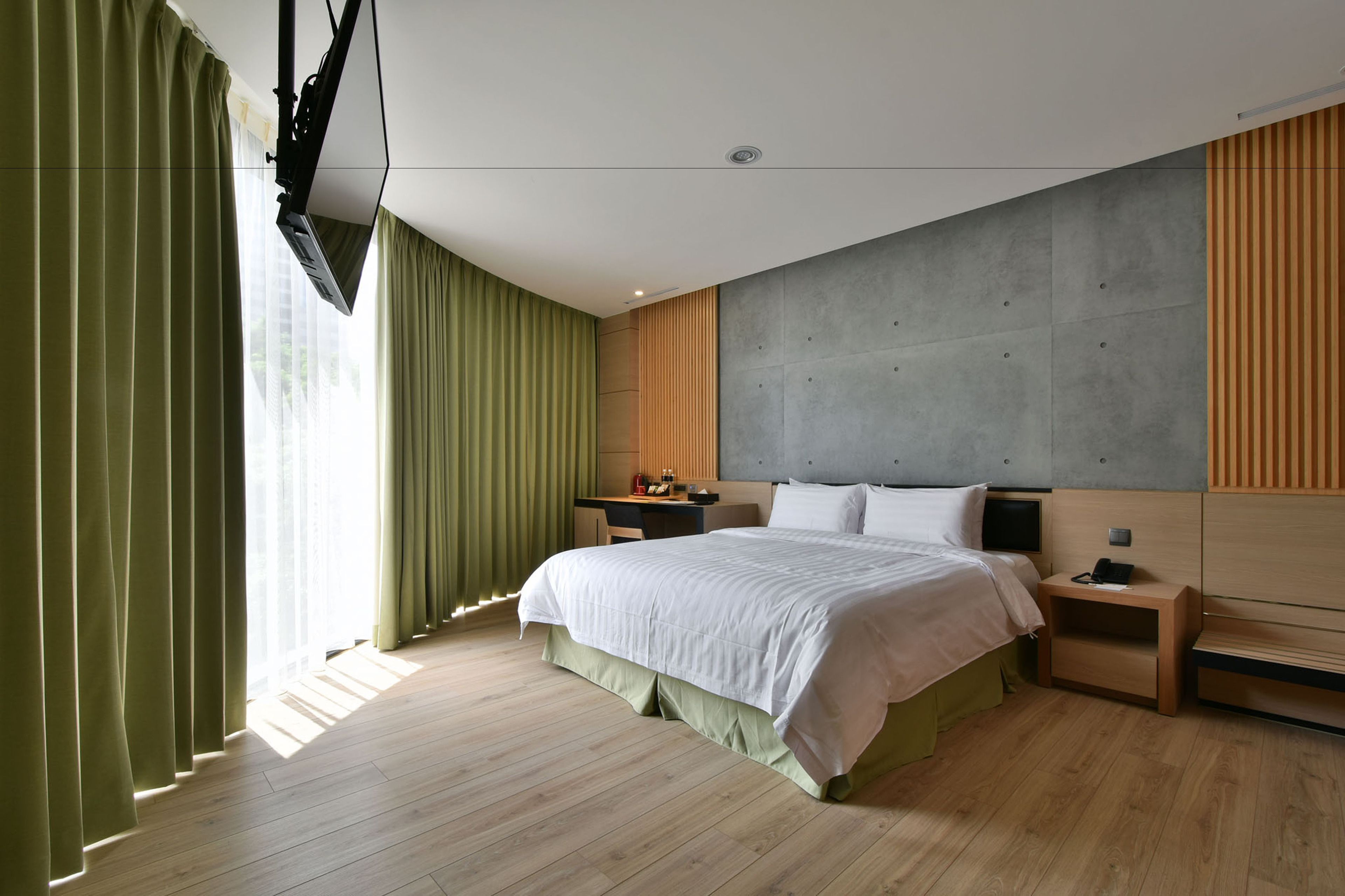Une chambre d’hôtel moderne avec un grand lit, un plancher en bois, un mur d’accent de couleur grise et un bureau avec une chaise.
