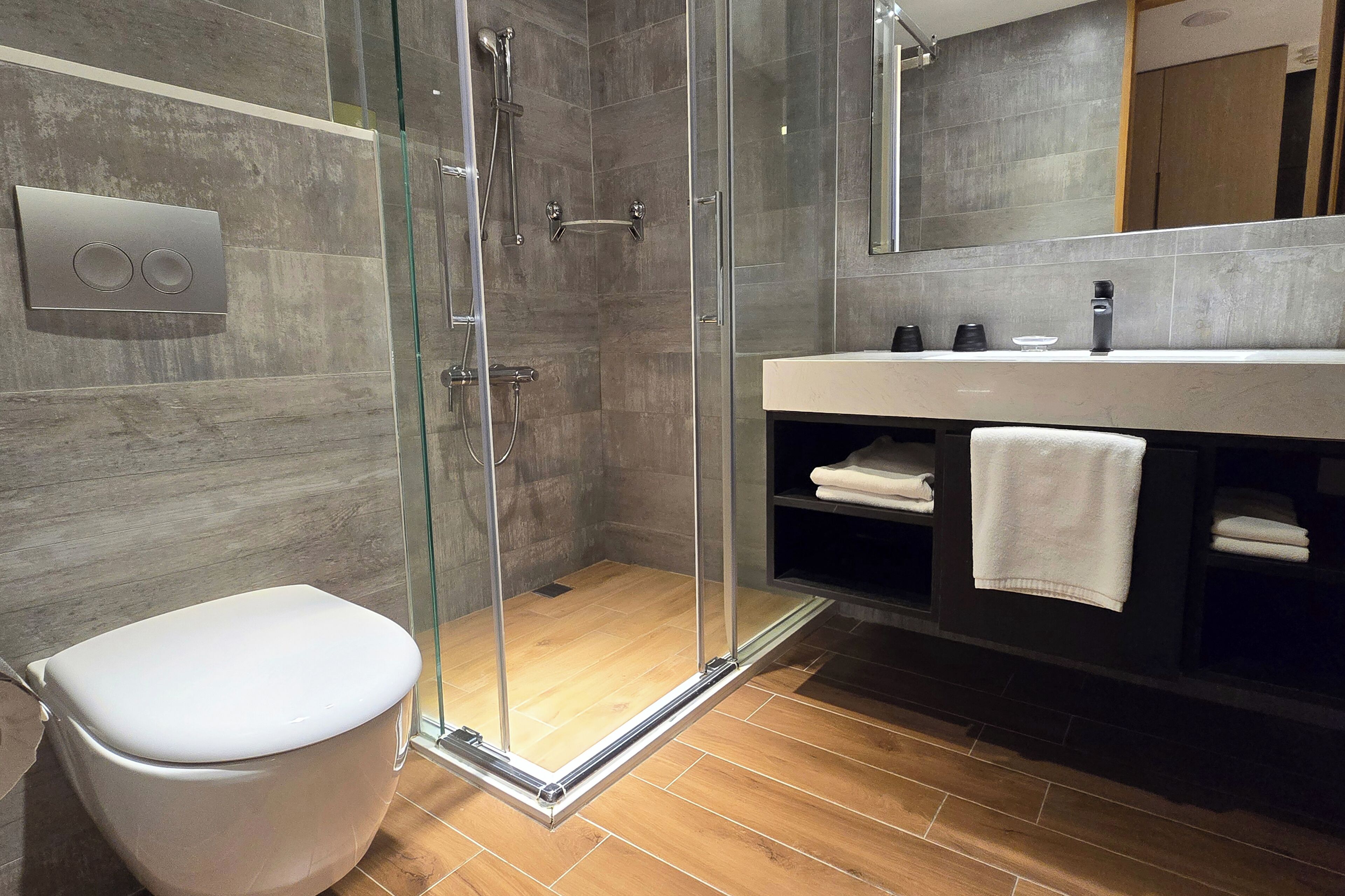 A modern bathroom with a glass-enclosed shower, a white toilet, and a vanity with a towel rack.