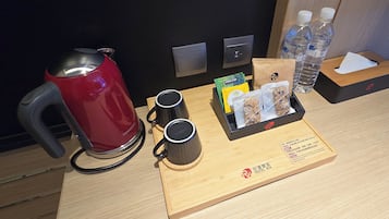 Ein Hotelzimmer mit einem Holftablett, das einen roten Wasserkocher, zwei schwarze Tassen, eine Taschentuchbox, eine kleine Tasche und zwei Wasserflaschen enthält.