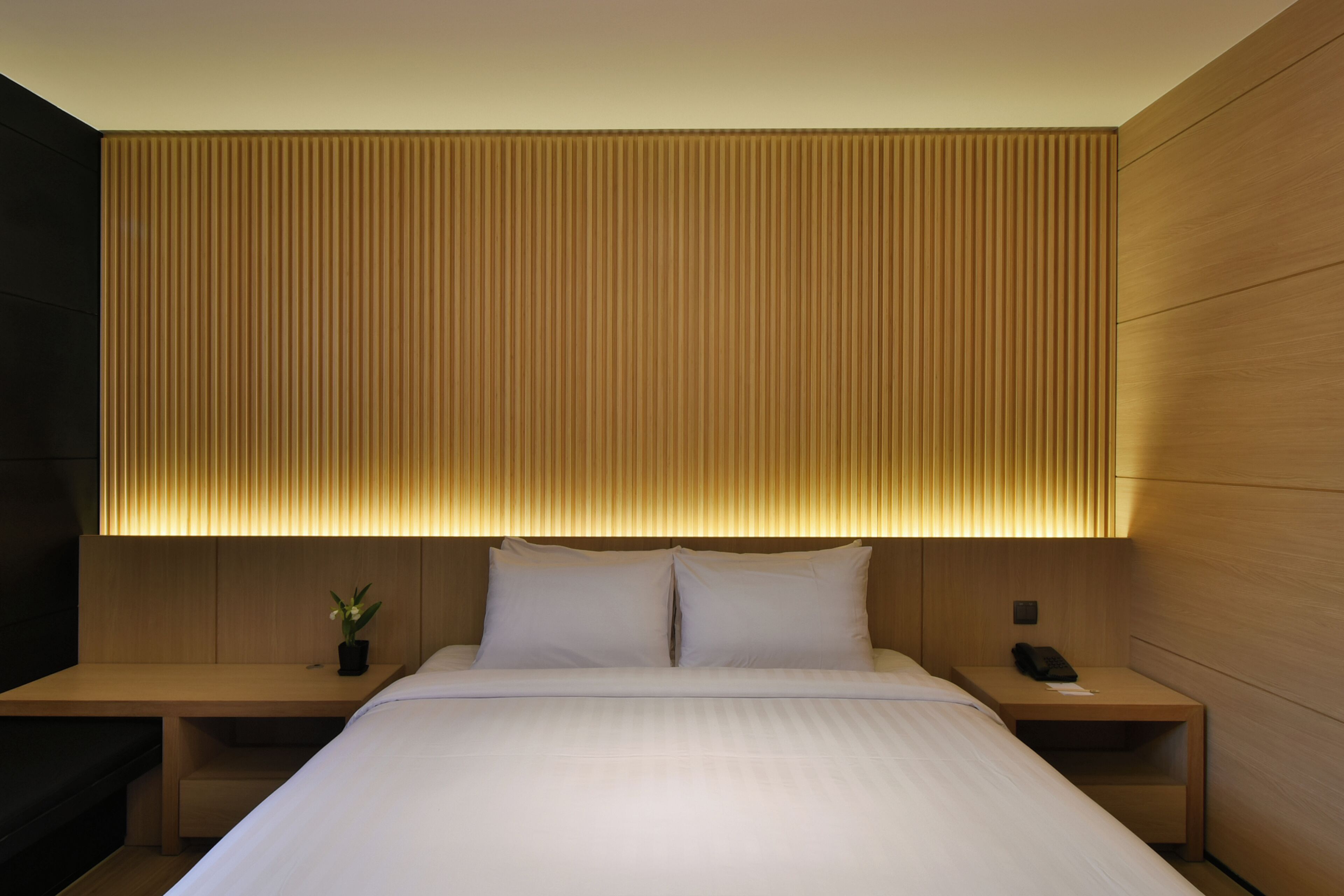 A modern hotel room with a large bed, bedside tables, and a wall-mounted light fixture.