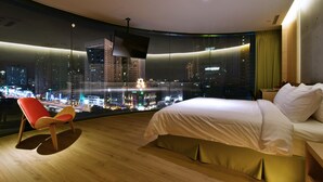 Habitació d'hotel moderna amb un llit gran, una televisió i vista a una ciutat de nit.
