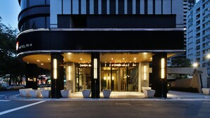 Entrada d'un hotel modern amb façana corbada, plantes en testos grans i zona d'entrada ben il·luminada.