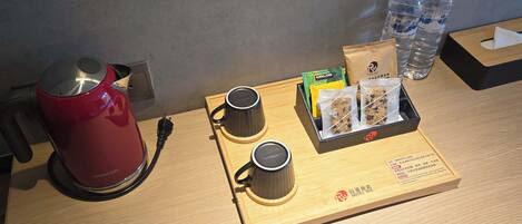 A hotel room with a red kettle, two cups, a tray with snacks and water bottles.