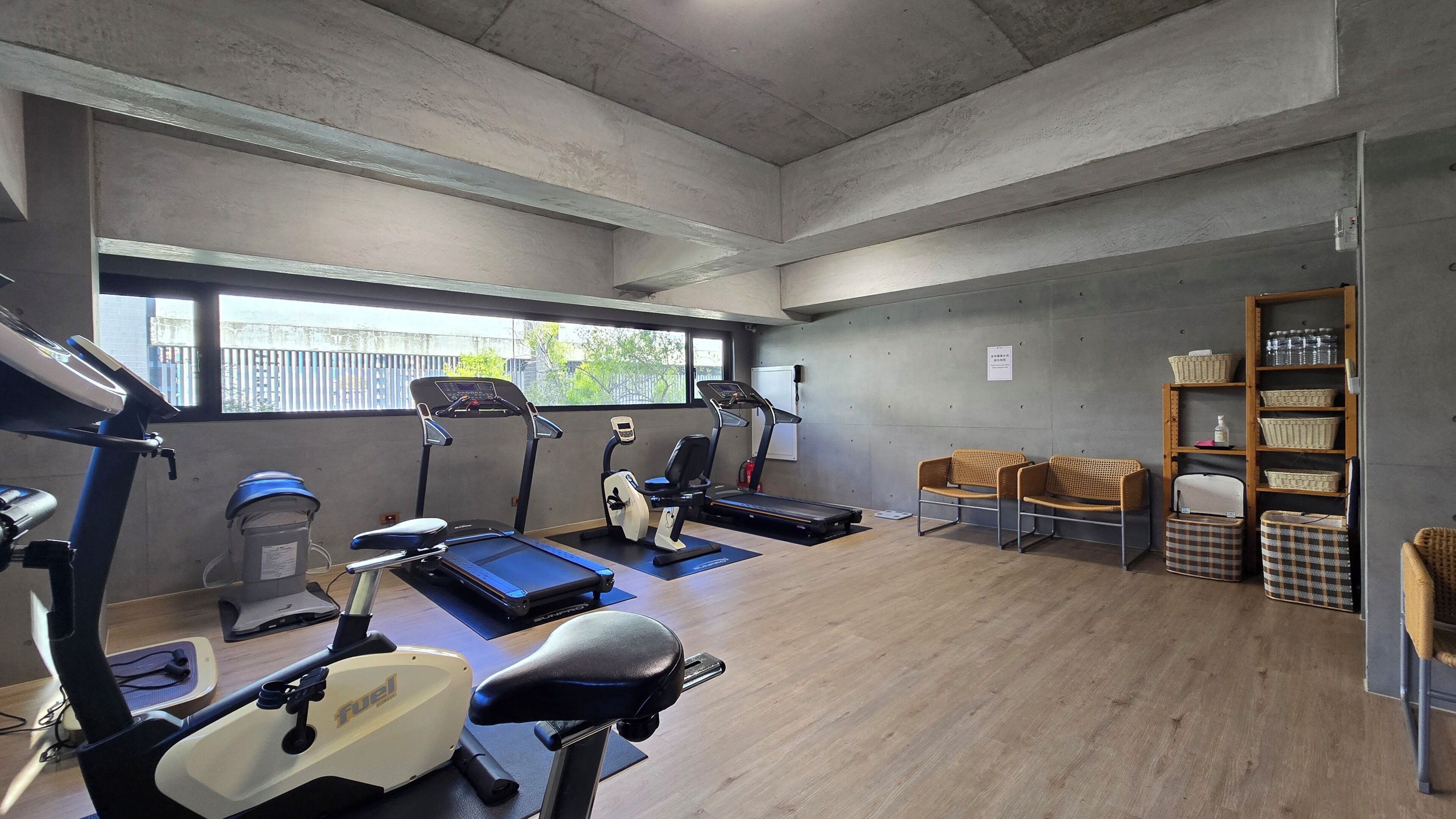 Ein Fitnessraum mit Trainingsgeräten, Holzboden und einem Fenster mit Blick nach draußen.