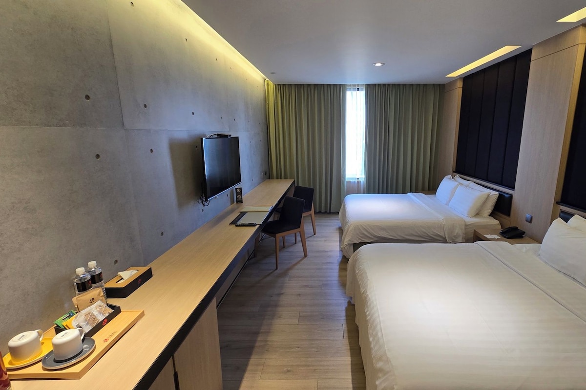 A hotel room with two beds, a desk with a chair, a television, and a window with curtains.