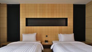 A hotel room with two beds, a wooden headboard, a small bedside table, and a black shelf above the beds.