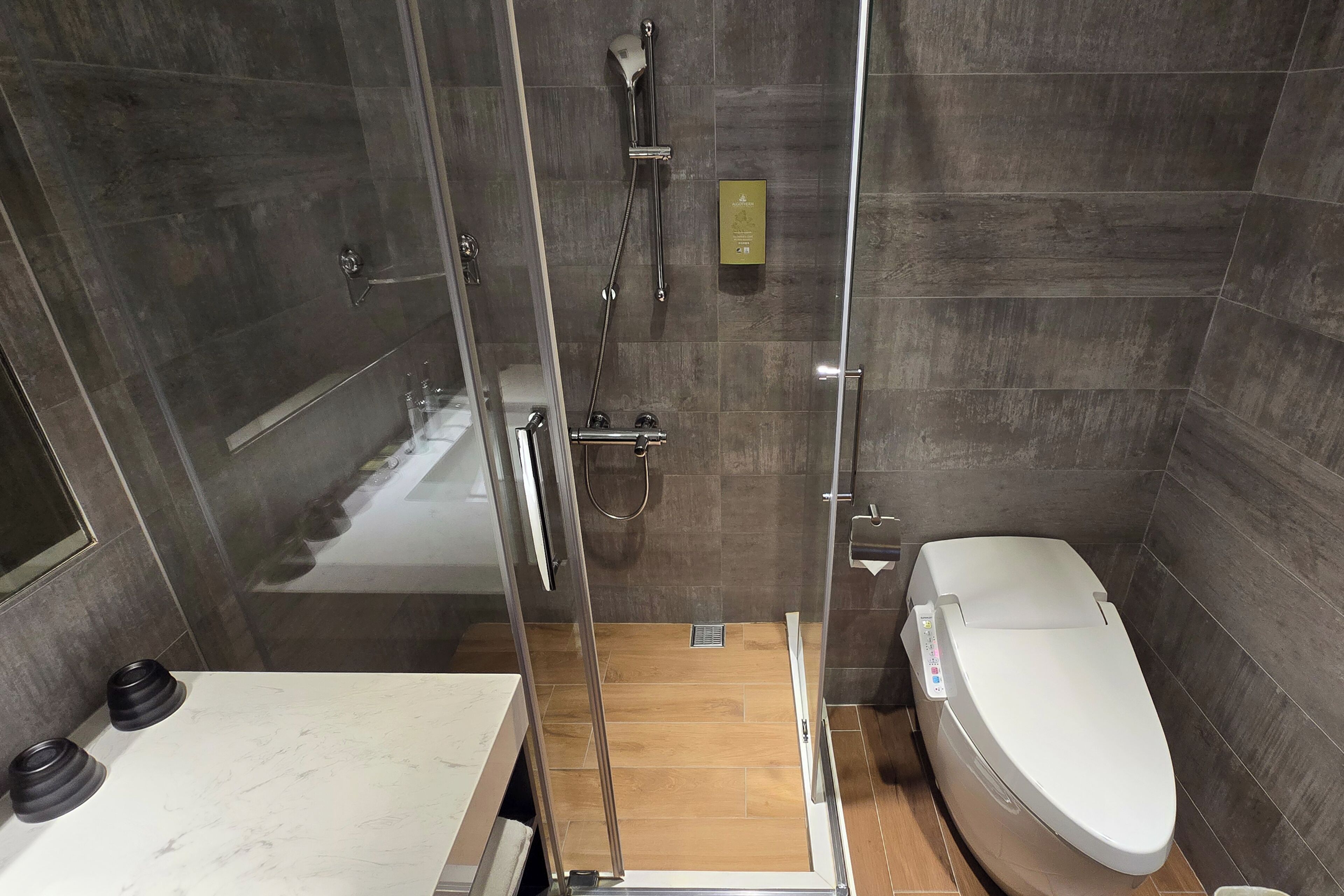 A modern bathroom with a glass-enclosed shower, a toilet, and a marble countertop.
