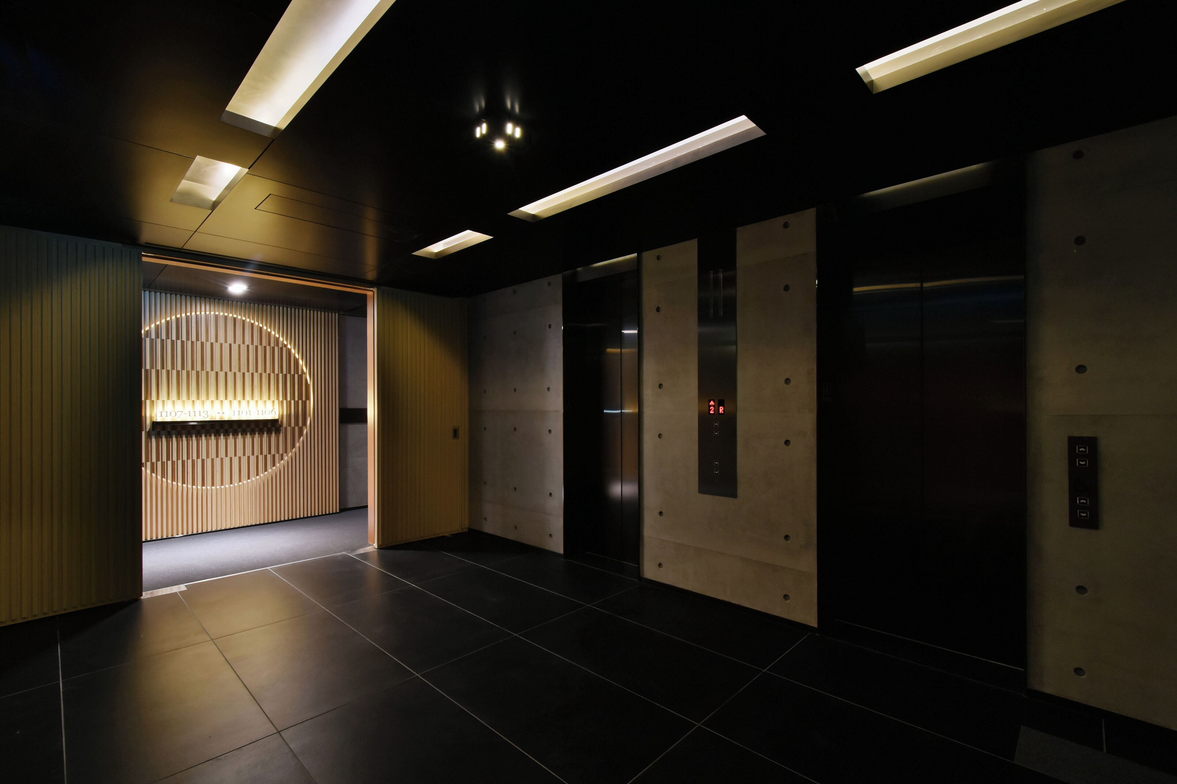 Un área de ascensores moderna con un mostrador de recepción de madera, una pantalla digital de ascensor y suelo de baldosas.