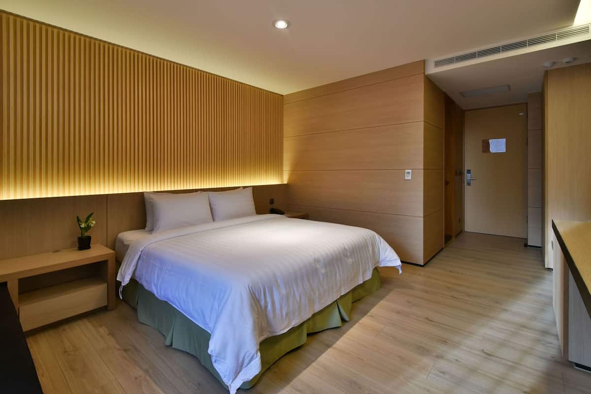 A modern hotel room with a large bed, a bedside table, and a built-in headboard.